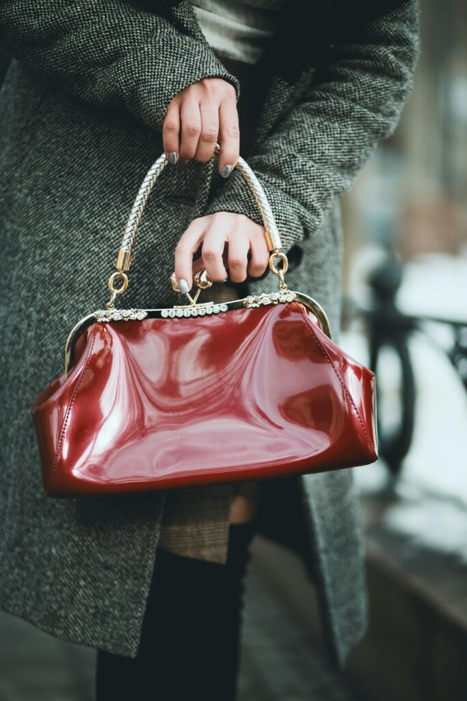 A stylish woman holds a shiny red leather handbag outdoors, showcasing fashion elegance.