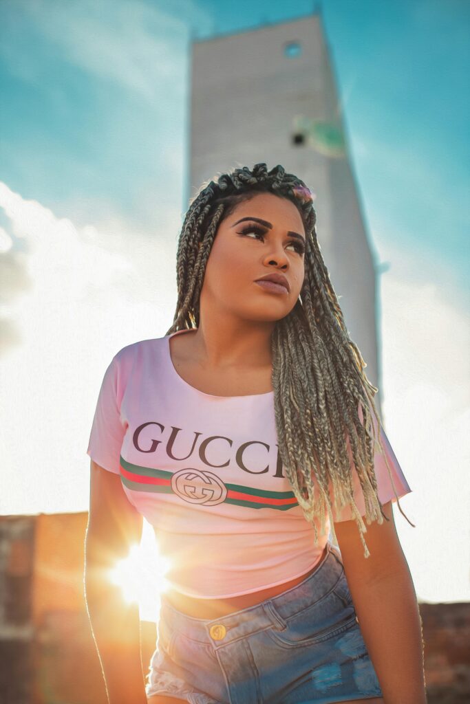 A stylish woman with braided hair poses confidently against a bright sky in Toritama, Brazil.